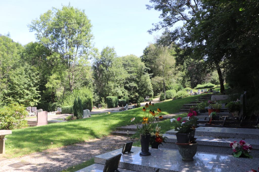 Vue du cimetière paysager du Mont-Dore avec des tombes au premier plan, de la pelouse et beaucoup d'arbres