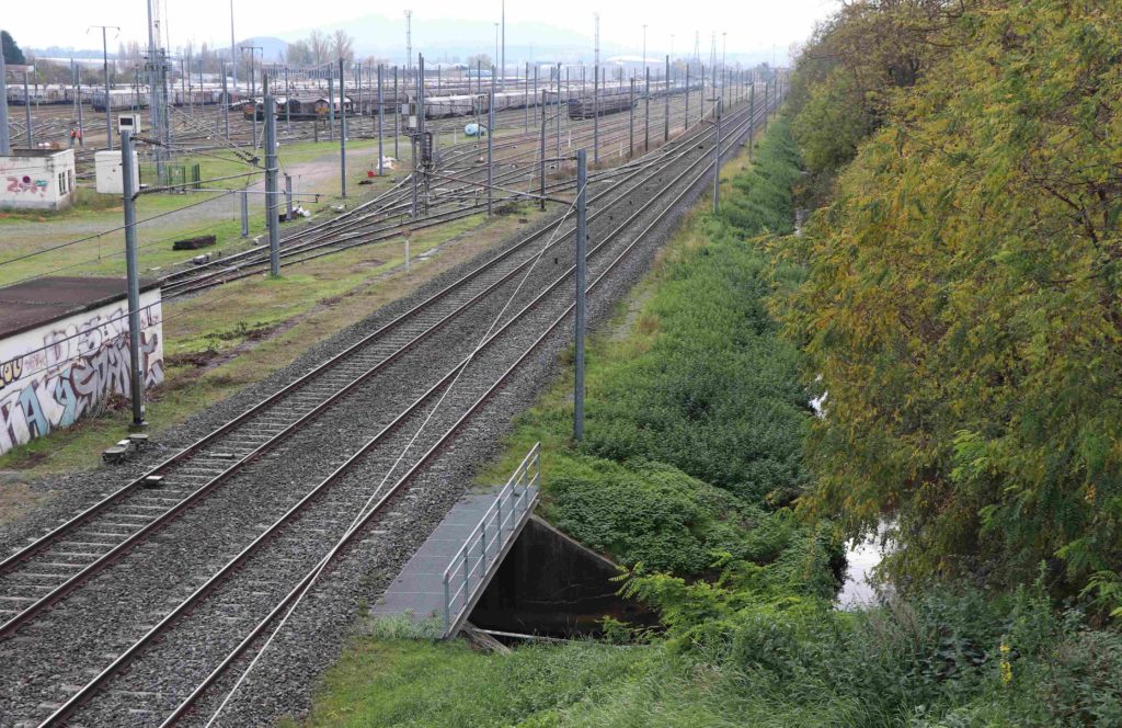 Vue sur les voies ferrées depuis un pont, avec le ruisseau qui passe dessous