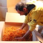 Dominique plongeant les mains dans un carton rempli de fleurs de calendula