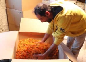 Dominique plongeant les mains dans un carton rempli de fleurs de calendula